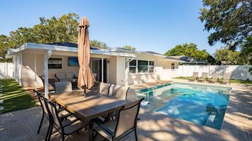 A poolside area with a dining table, chairs, and a covered umbrella.