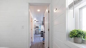 Un pasillo estrecho con paredes blancas y suelo de madera que conduce a una zona de cocina.