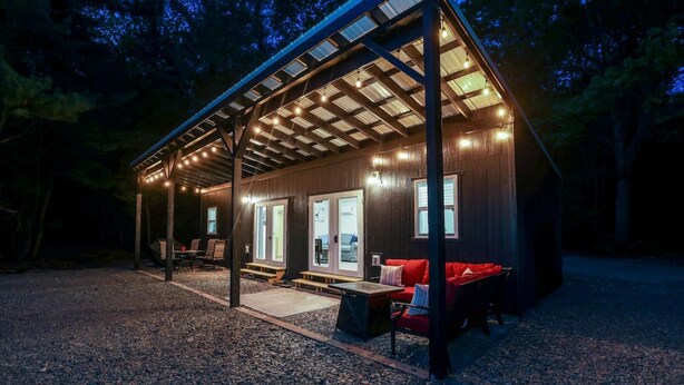 Una cabaña de madera con un porche cubierto, mobiliario exterior y un sofá rojo.