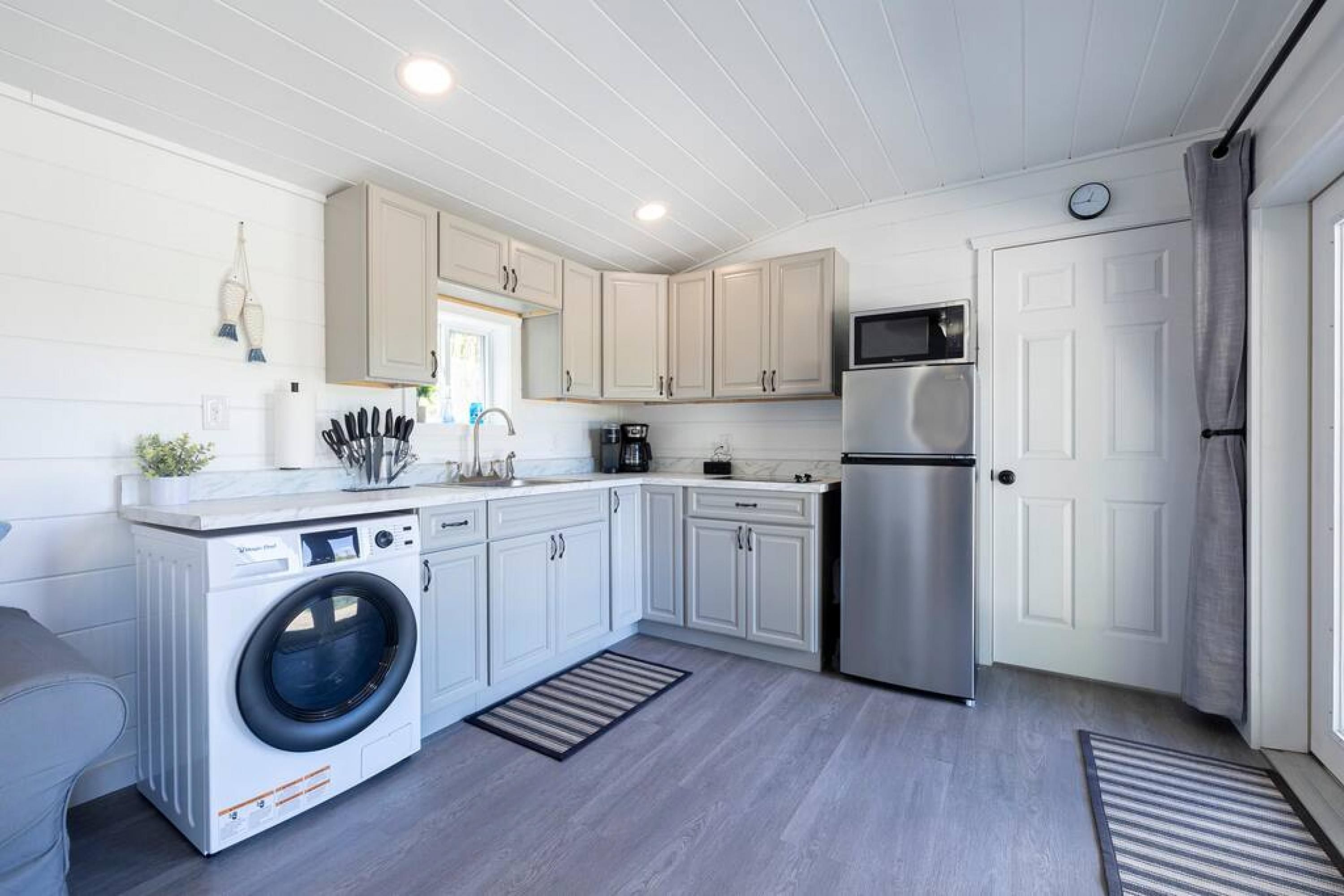 A compact kitchen with white cabinets, a stainless steel refrigerator, a washing machine, and a microwave.