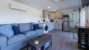 Un espacio habitable funcional con sofá, mesa de centro, lavadora, microondas y refrigerador.