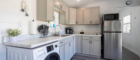 Una cocina funcional con armarios blancos, un refrigerador de acero inoxidable, una lavadora y un microondas.