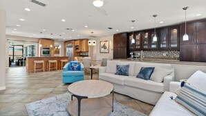 A spacious living area with a large sofa, a round coffee table, and a blue armchair. There is a kitchen area with dark wooden cabinets and a tiled backsplash. - Heated Pool Home Pool Table Spacious Family (Largo)
