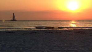Escena de playa con un velero en el agua durante el atardecer.