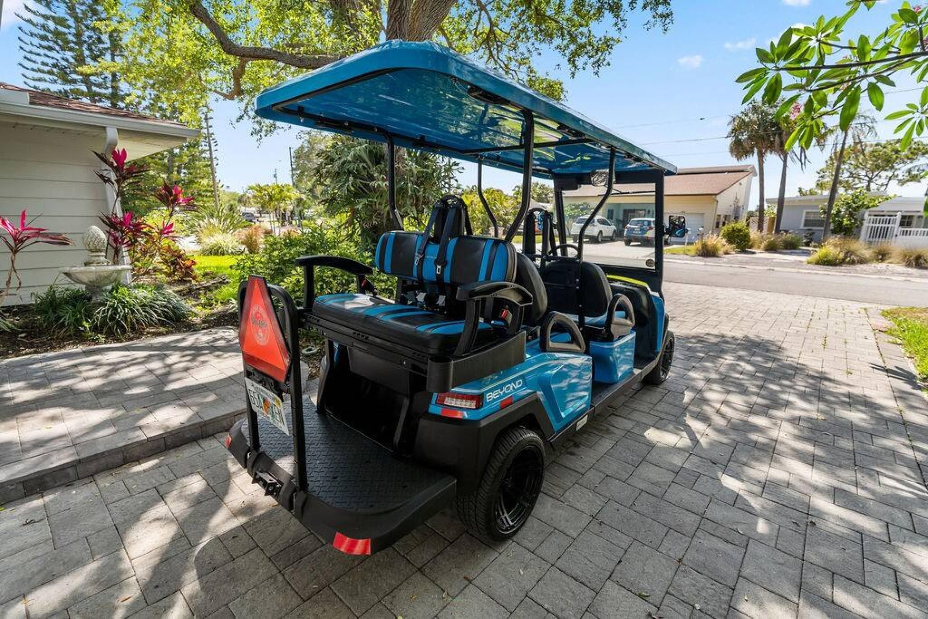 A golf cart parked on a paved driveway with a covered canopy, surrounded by lush greenery and residential buildings.