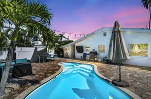 Une piscine avec une terrasse carrelée, du mobilier d’extérieur et un espace barbecue.