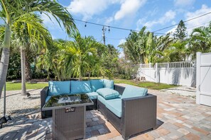 Une terrasse dotée d’un canapé modulable et d’une table à plateau en verre, entourée de palmiers et d’une clôture blanche.