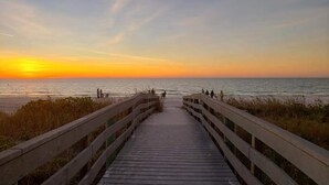 En träpromenad som leder till en strand, med en solnedgång i bakgrunden.