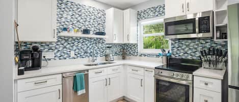 A modern kitchen with white cabinets, a tiled backsplash, a built-in microwave, a stove, and a dishwasher.