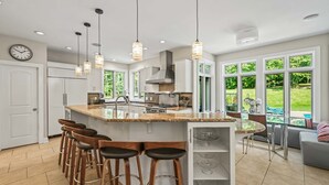A modern kitchen with a large island, bar stools, pendant lighting, and a view of the garden. - Secluded Lux Mansion Pool Home With Amazing Views (Nassau)