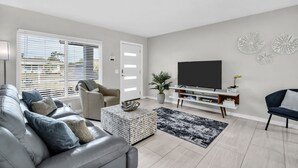 A modern living room with a sofa, TV, and decorative wall pieces. - Pool Hottub 5 Miles Clearwater IRB Pet Friendly (Clearwater)
