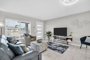 A modern living room with a sofa, TV, and decorative wall pieces. - Pool Hottub 5 Miles Clearwater IRB Pet Friendly (Clearwater)