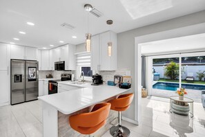 Una cocina moderna con armarios blancos, electrodomésticos de acero inoxidable y una isla grande con taburetes de bar.