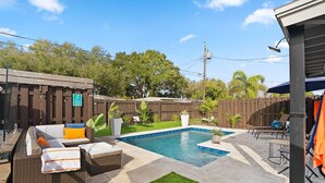A backyard with a swimming pool, outdoor seating, and a fenced area.