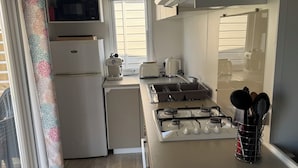 Cocina compacta con microondas, tostadora y estufa, refrigerador y ventana con persianas.