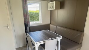 Una habitación pequeña con una mesa de madera, sillas blancas, un banco y un mueble bajo.