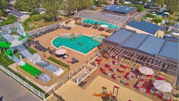 Vista aérea de un resort con piscina, toboganes acuáticos y zona de playa con tumbonas y sombrillas.