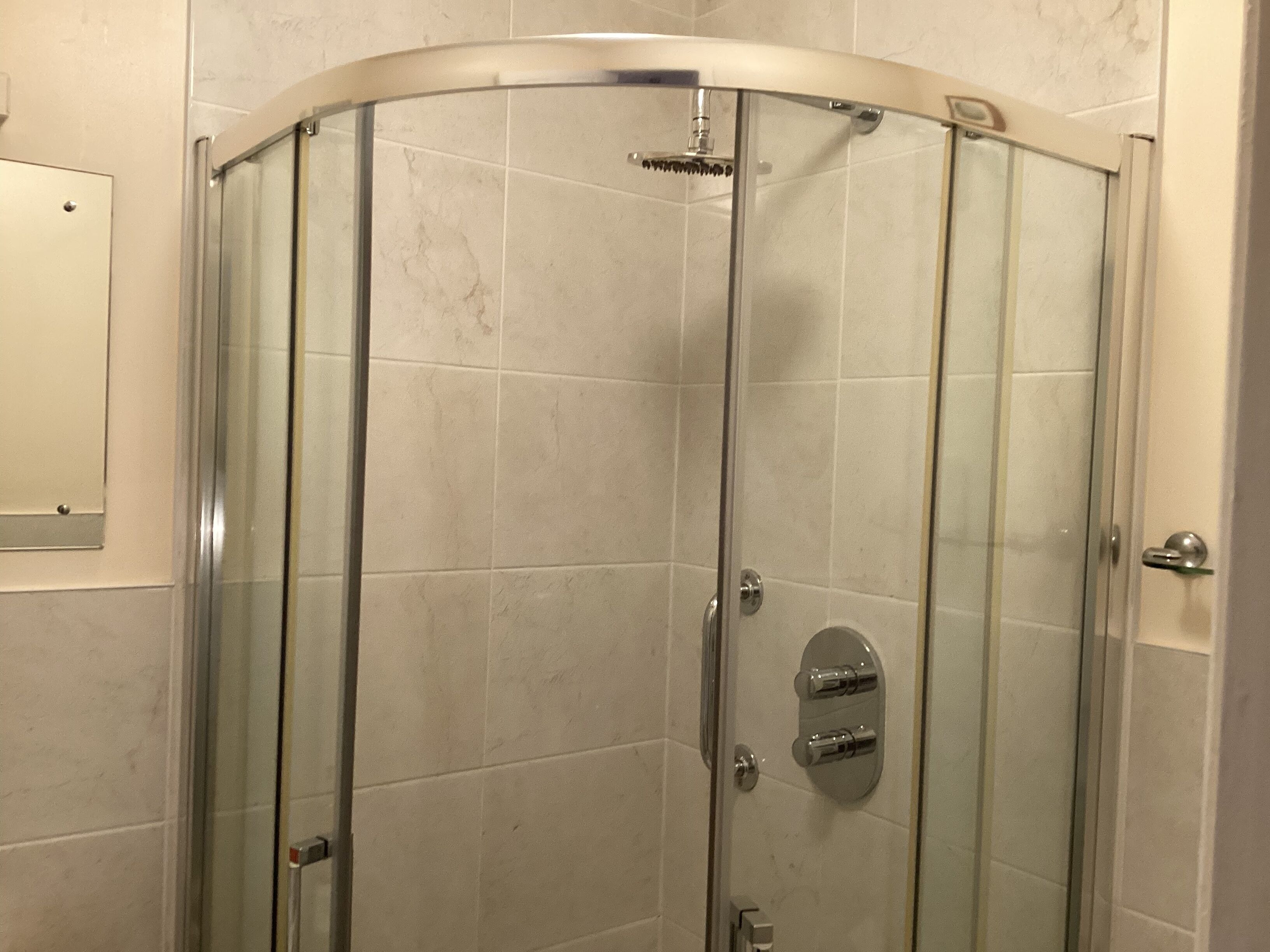 A glass-enclosed shower stall with a curved door, a wall-mounted towel rack, and a door handle.