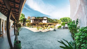A courtyard with a building featuring a balcony and potted plants. - Pousada El Camenito (Búzios)
