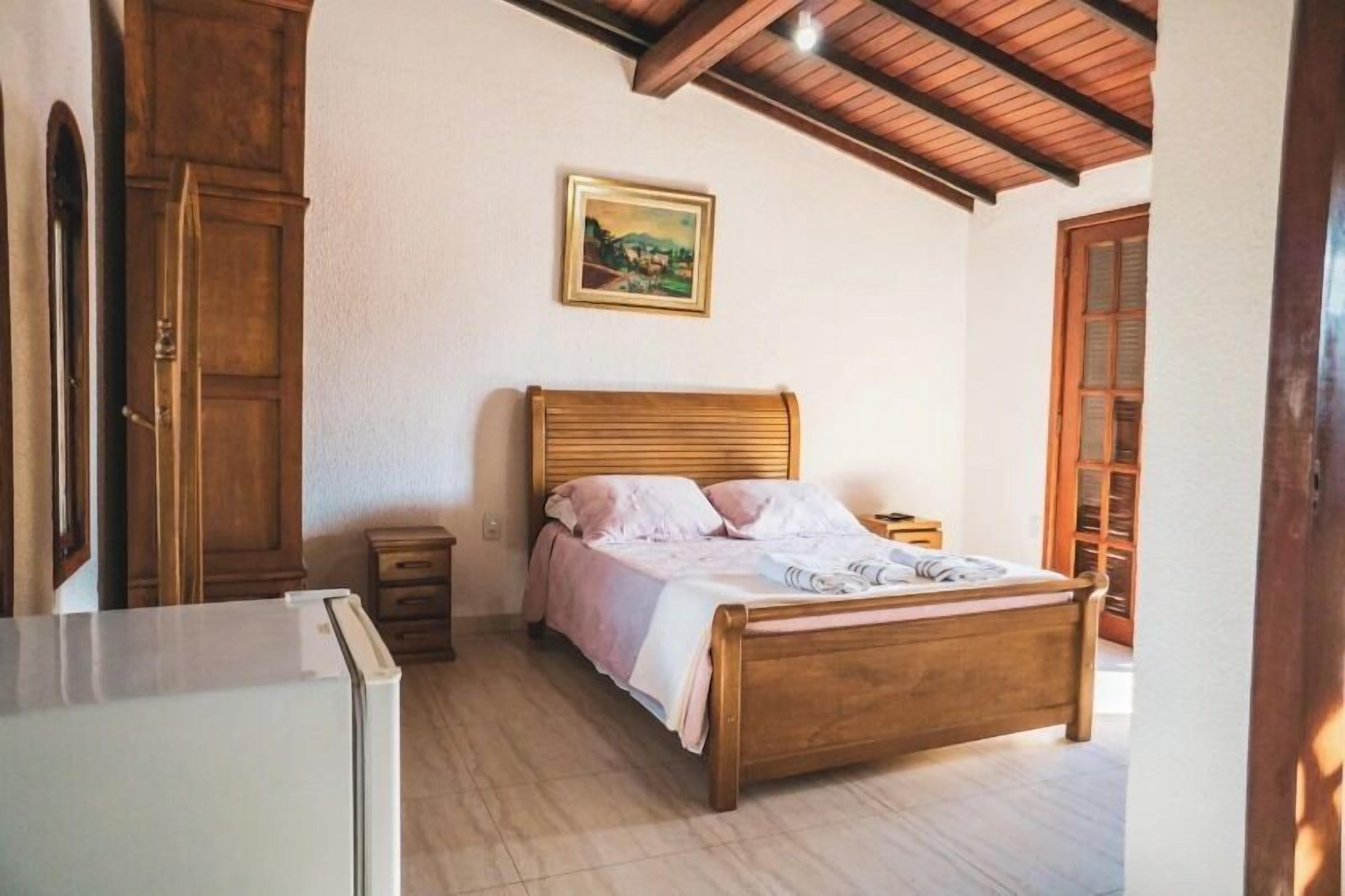 A bedroom with a wooden bed, a nightstand, a dresser, and a painting on the wall.