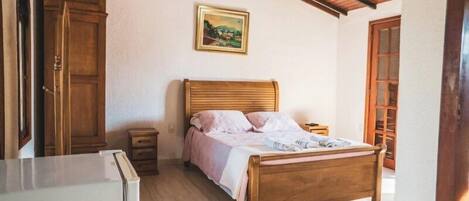 A bedroom with a wooden bed, a nightstand, a dresser, and a painting on the wall.
