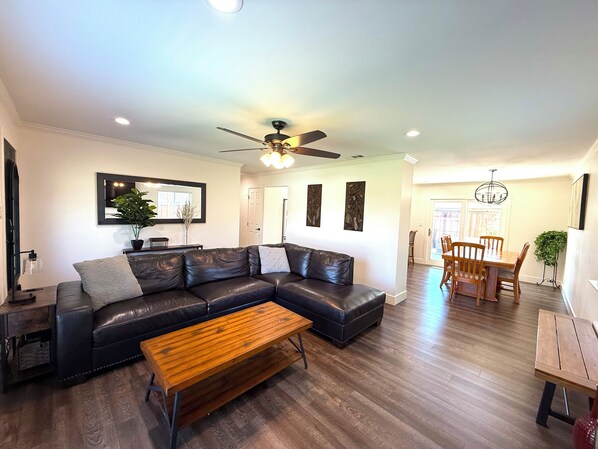 A modern living room with a sectional sofa, a wooden coffee table, and a dining area with wooden chairs and a table. - 3bd/2ba Remodeled Luxury Home + Steam Shower! (Concord)