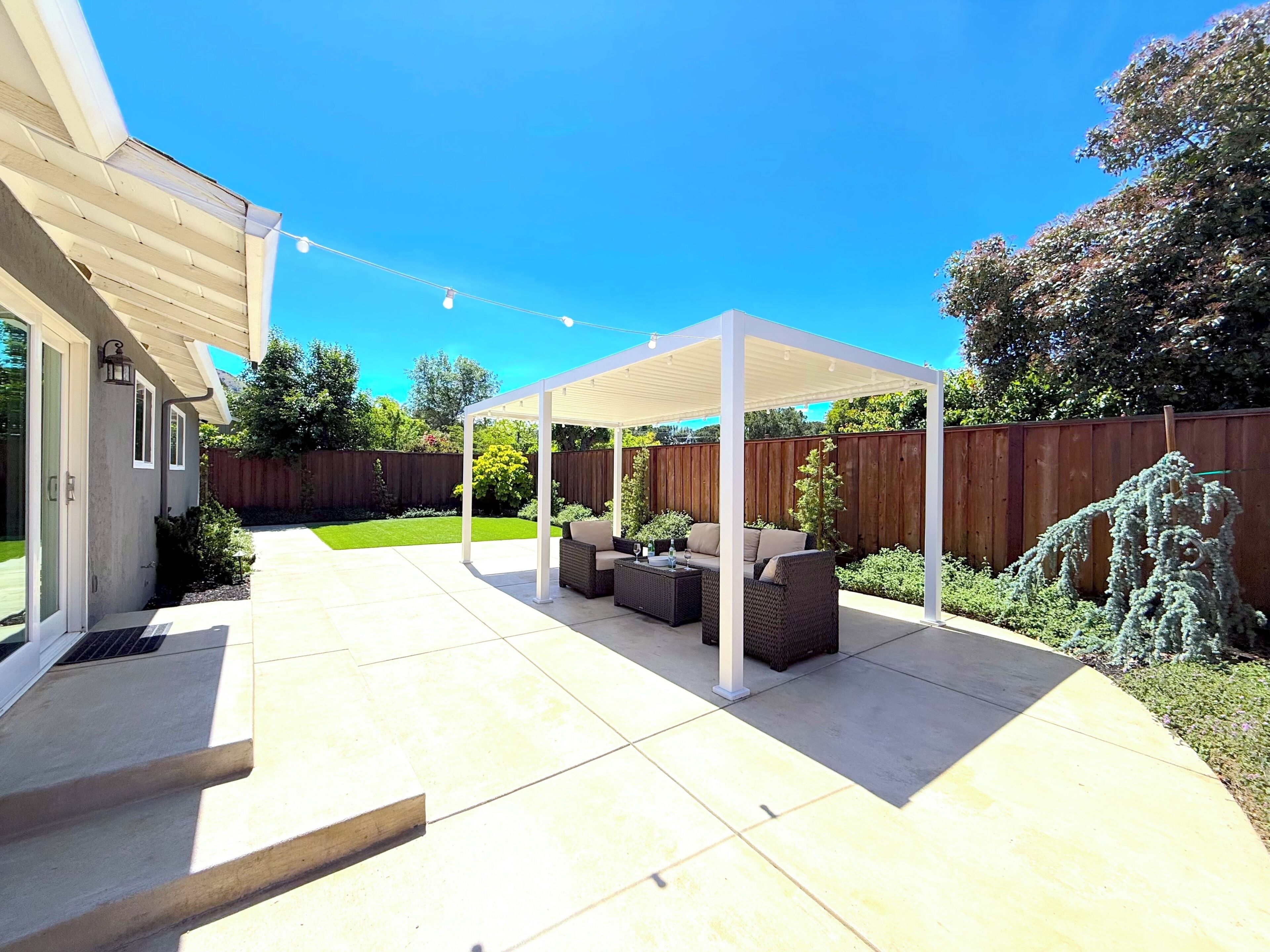 Une terrasse couverte, aménagée avec du mobilier d’extérieur, une clôture en bois et une pelouse bien entretenue.