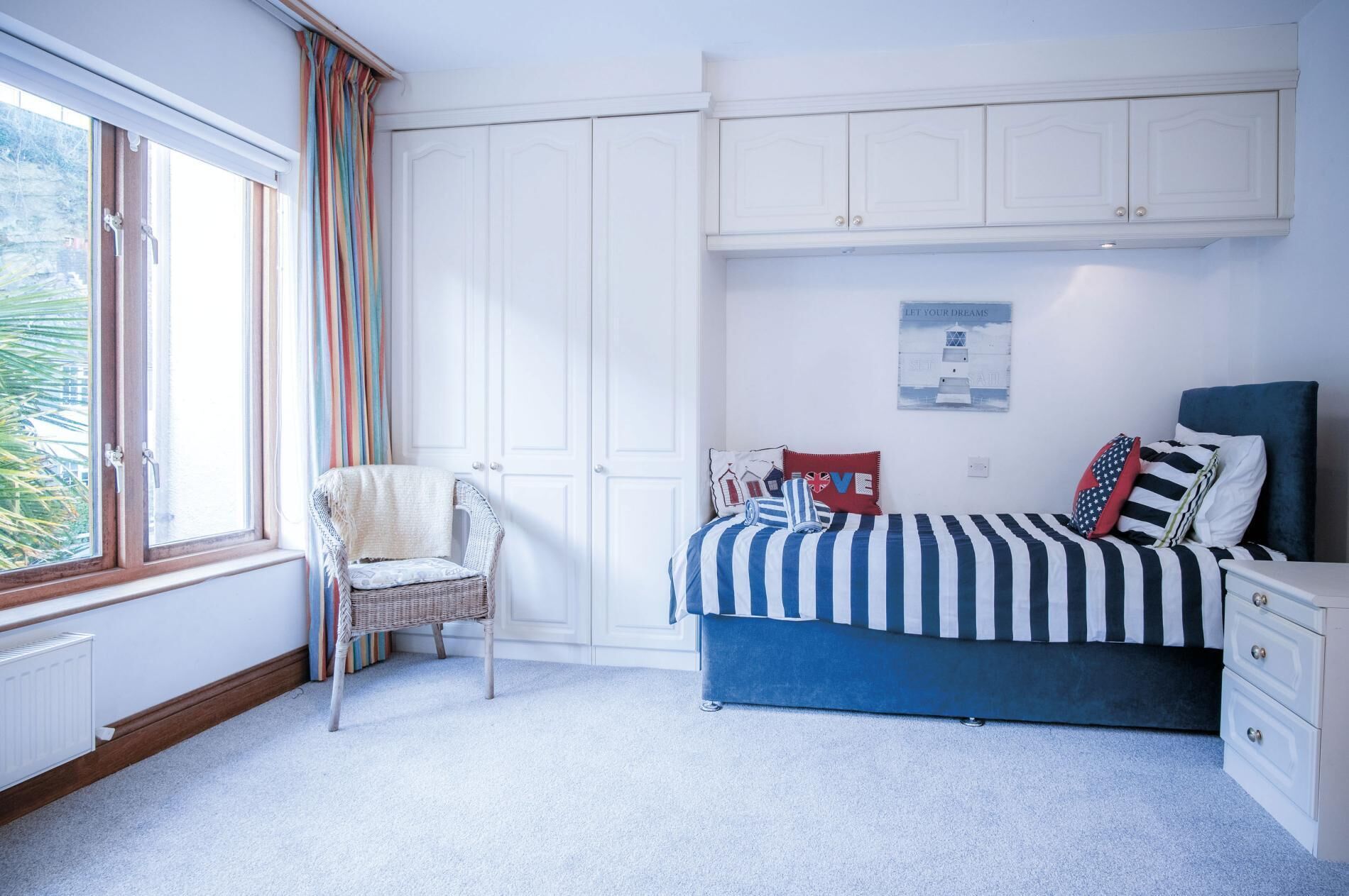 A bedroom with a bed, a chair, a dresser, and a window with curtains.