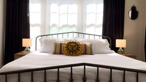 A bed with white bedding, a sun-shaped pillow, and a striped pillow. There are two bedside lamps on wooden nightstands.