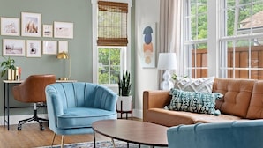 A living room with a blue armchair, a brown sofa, a coffee table, and a window with a view of greenery.