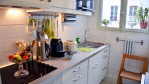 Une cuisine moderne avec des meubles blancs, une cuisinière en acier inoxydable et une fenêtre donnant sur la rue.