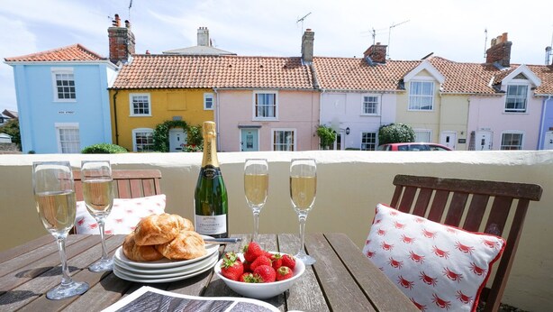 A terrace with a table set for a meal, including croissants, strawberries, and champagne glasses. - The Corner Cottage (Aldeburgh)