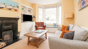 A cozy living room with a fireplace, a sofa, a coffee table, and a television. - The Corner Cottage (Aldeburgh)