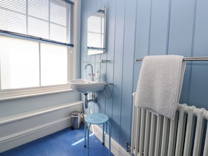 A bathroom with a white sink, a mirror, a towel rack, a radiator, and a blue floor. - The Corner Cottage (Aldeburgh)