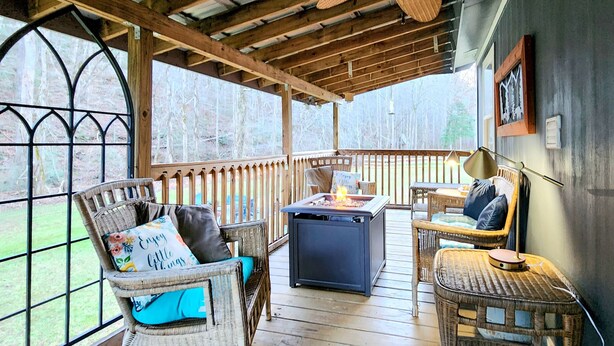 A covered porch with wicker furniture, a fire pit, and a view of the surrounding forest. - Bungalow+RV/10 acres/Stream/Sleeps6 (Ellijay)