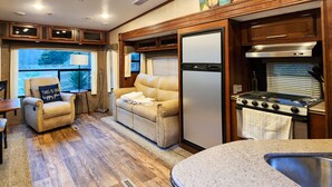A compact RV kitchen with a stove, refrigerator, and seating area. - Bungalow+RV/10 acres/Stream/Sleeps6 (Ellijay)