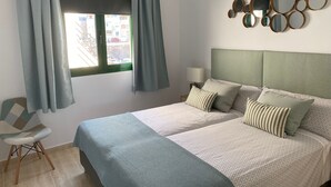 Une chambre à coucher avec un lit, deux oreillers, une chaise, une table de chevet, une lampe et une fenêtre avec des rideaux.