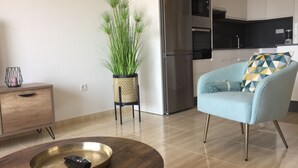 Un salon moderne comprenant un canapé, une table basse, une plante en pot et un coin cuisine équipé d’appareils électroménagers.