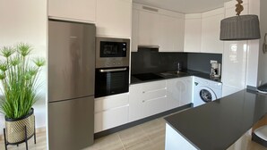 Une cuisine moderne avec des armoires blanches, un réfrigérateur en acier inoxydable, un four encastré, un four à micro-ondes, un évier, une machine à café et un lave-linge.
