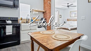 Una cocina moderna con un pilar de ladrillo, un microondas, una estufa y un comedor con mesa de madera y sillas blancas.