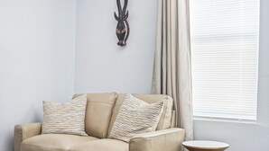 Un salón con sofá color beige, cojines estampados, una mesita redonda y un adorno en la pared.