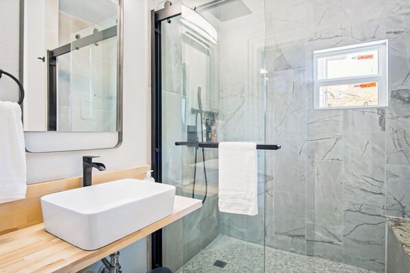 A modern bathroom with a white sink, a glass shower enclosure, and a marble wall.
