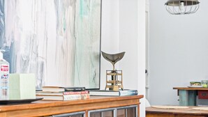Una habitación con un escritorio de madera, libros, una lámpara y un cuadro abstracto grande en la pared.