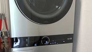 Una lavadora y secadora apiladas, con un panel de control y un tubo de entrada de agua visible.