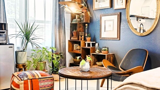 Un salón acogedor con una mesa redonda de madera, un sillón cómodo y una estantería llena de libros y objetos decorativos.