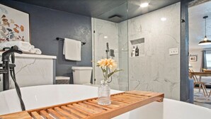Uma casa de banho moderna com uma banheira independente, um tabuleiro de madeira e um vaso com flores.