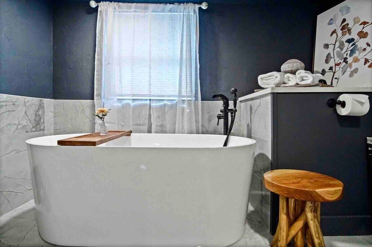 Une salle de bain moderne avec une baignoire sur pieds, un tabouret en bois et un porte-serviettes.
