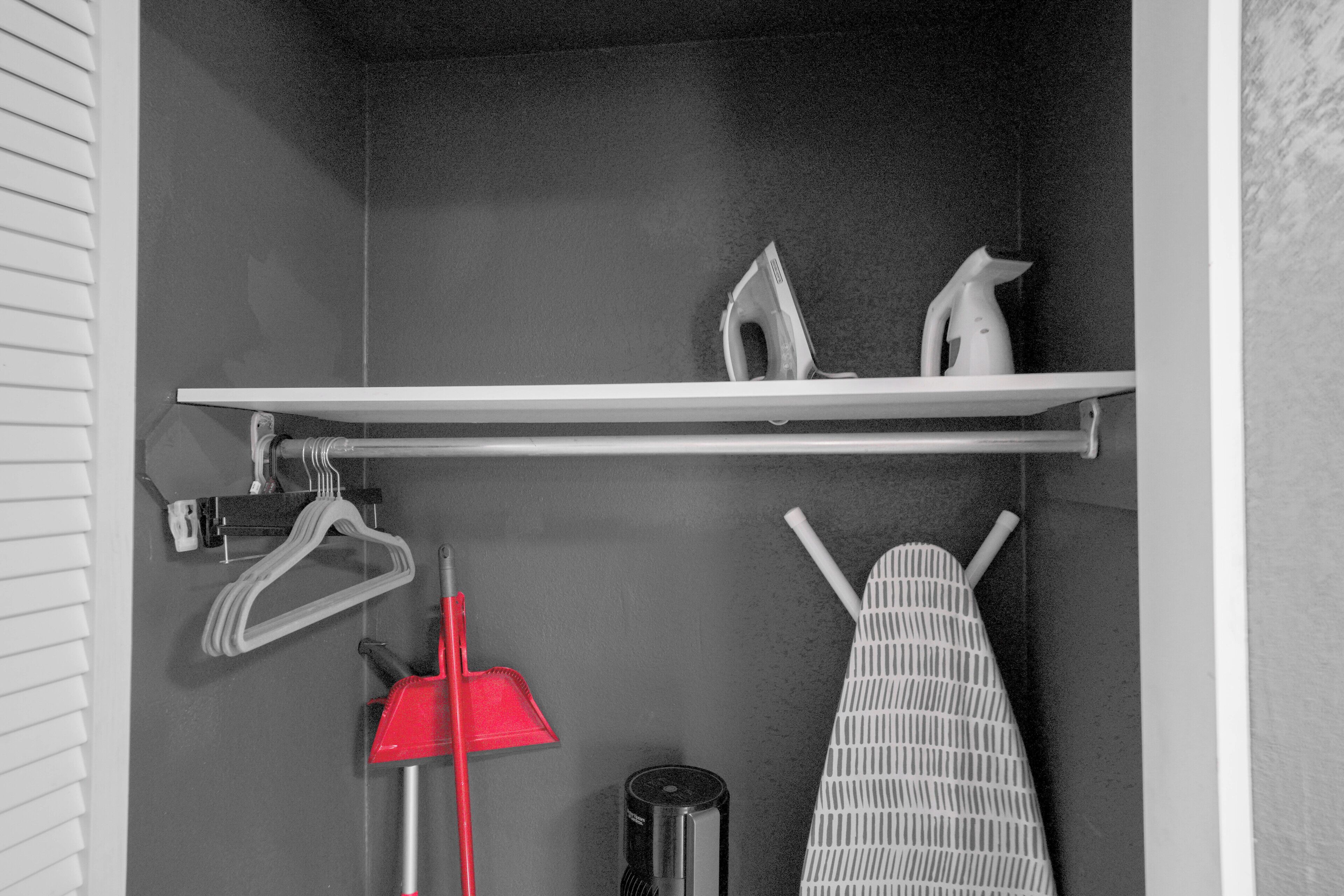 Ein Badezimmer mit Handtuchhalter, einer Bürste mit rotem Griff, einem weißen Bügelbrett und einem Regal mit einem weißen Bügeleisen und einer weißen Kanne.