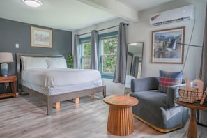 Une chambre à coucher avec un lit, une chaise, une table ronde en bois et une fenêtre avec des rideaux.