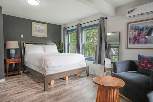 A bedroom with a bed, bedside table, chair, round table, and large windows.